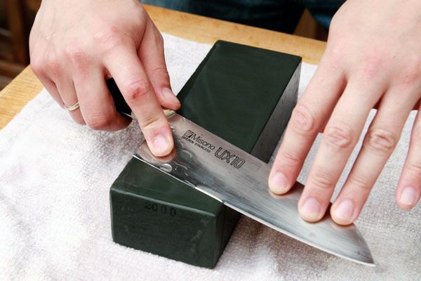 Hands sharpening a knife on a lower grit whetstone