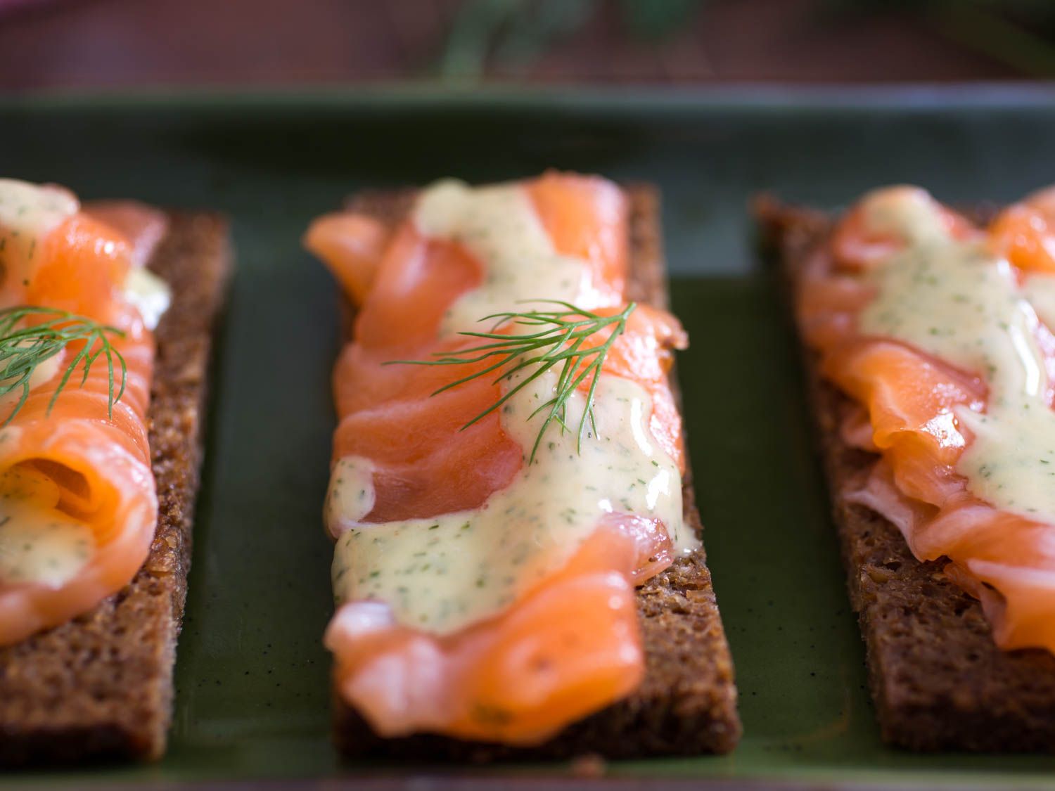 Gravlax on pumpernickel slices with a drizzle of mustard sauce and fresh dill garnish.