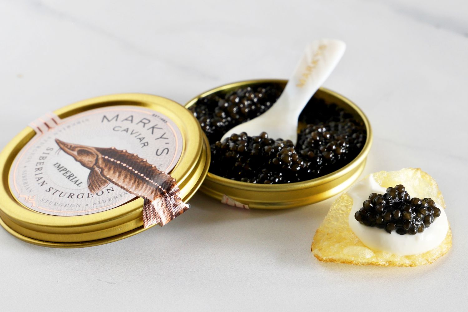 A tin of Imperial Sturgeon caviar from Marky's next to a potato chip topped with crème fraîche and caviar