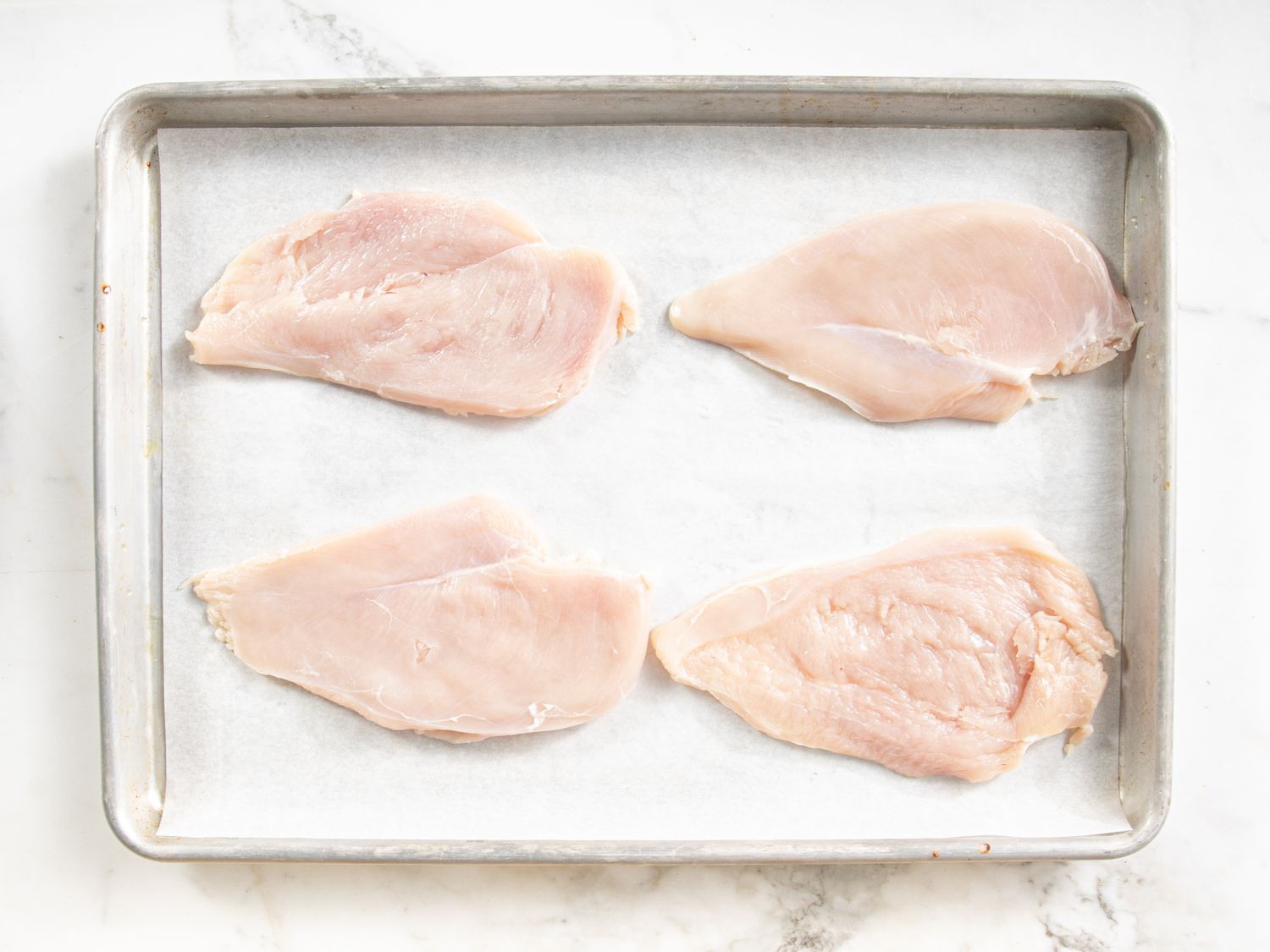 Overhead view of chicken cutlets resting on a baking sheet.