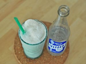Overhead shot a tall glass vanilla ice cream soda and straw with a bottle seltzer on the side.