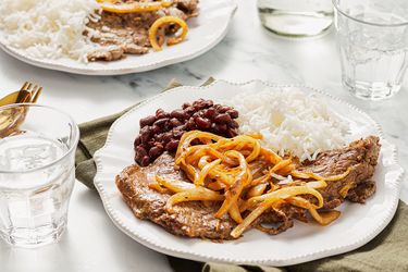 Plate with steak, cooked onions, rice, and beans on a table setting