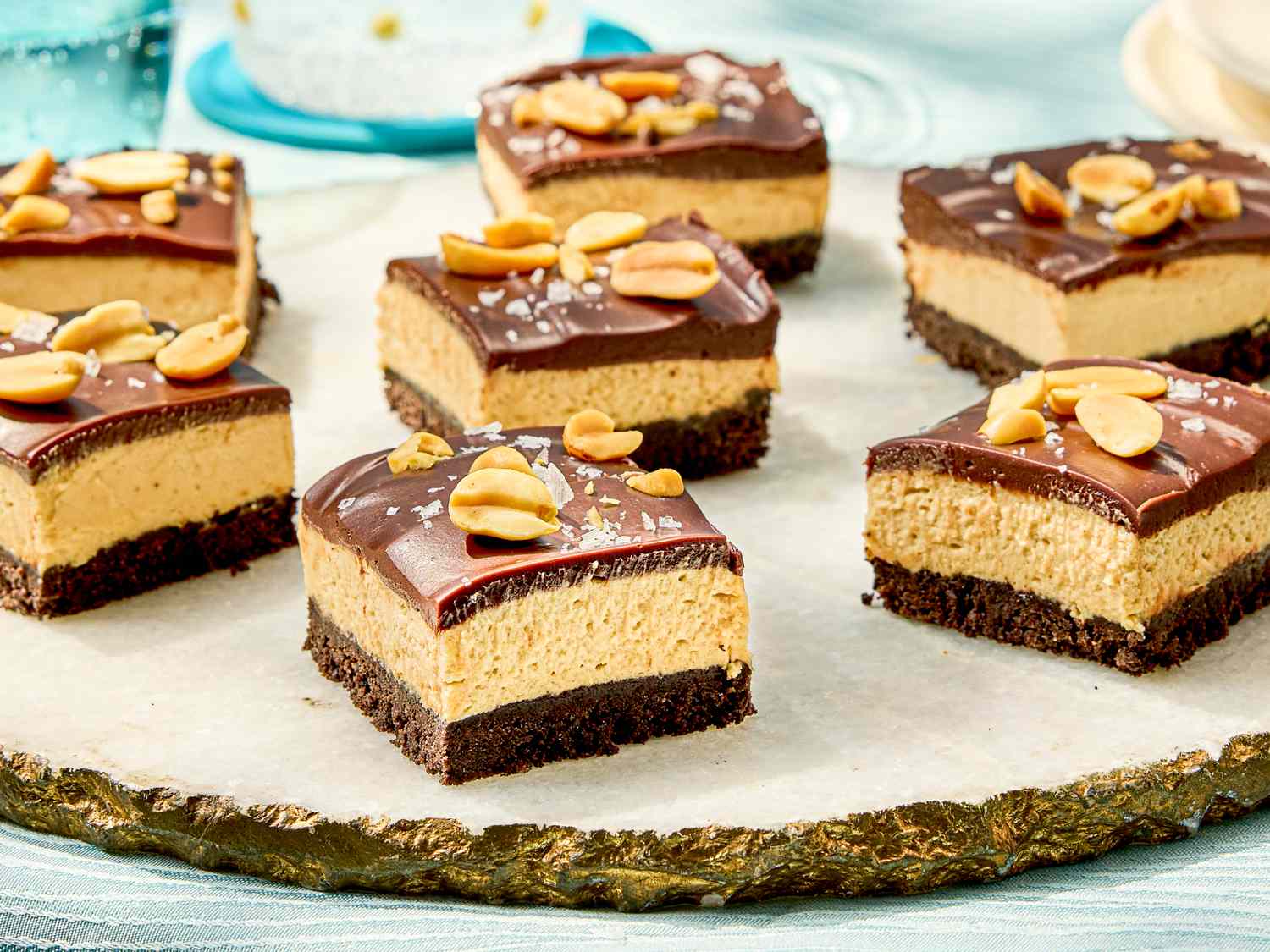 Chocolate peanut butter cheesecake bars garnished with peanuts arranged on a serving plate