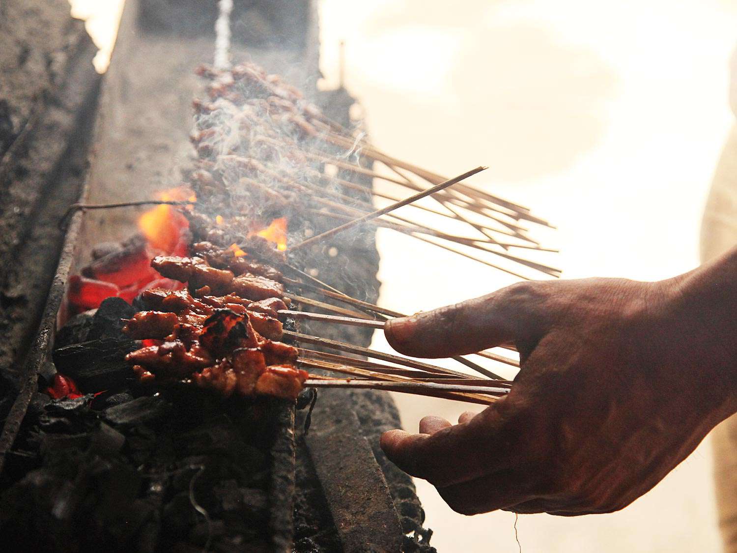Skewers of pork satay being cooked over hot coals in Bali, Indonesia.