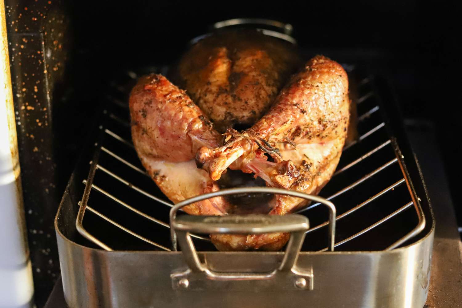 A roasted turkey in a stainless steel roasting pan inside an oven showing the bird resting on a rack
