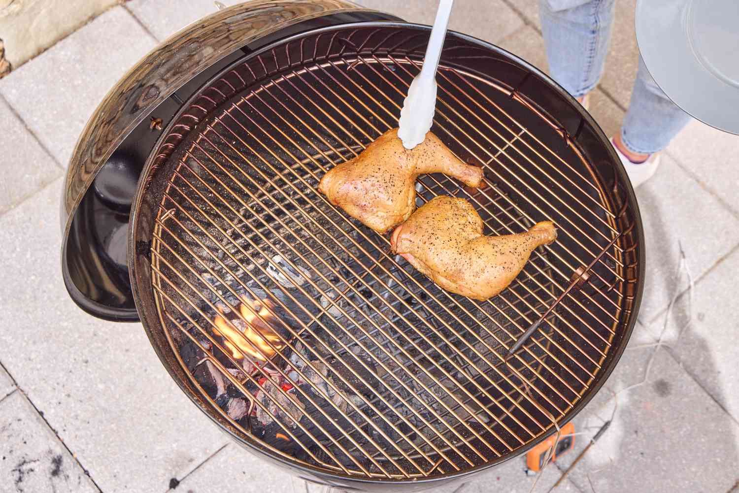Tongs grasping chicken on the Weber Original Kettle Premium 22-Inch Charcoal Grill