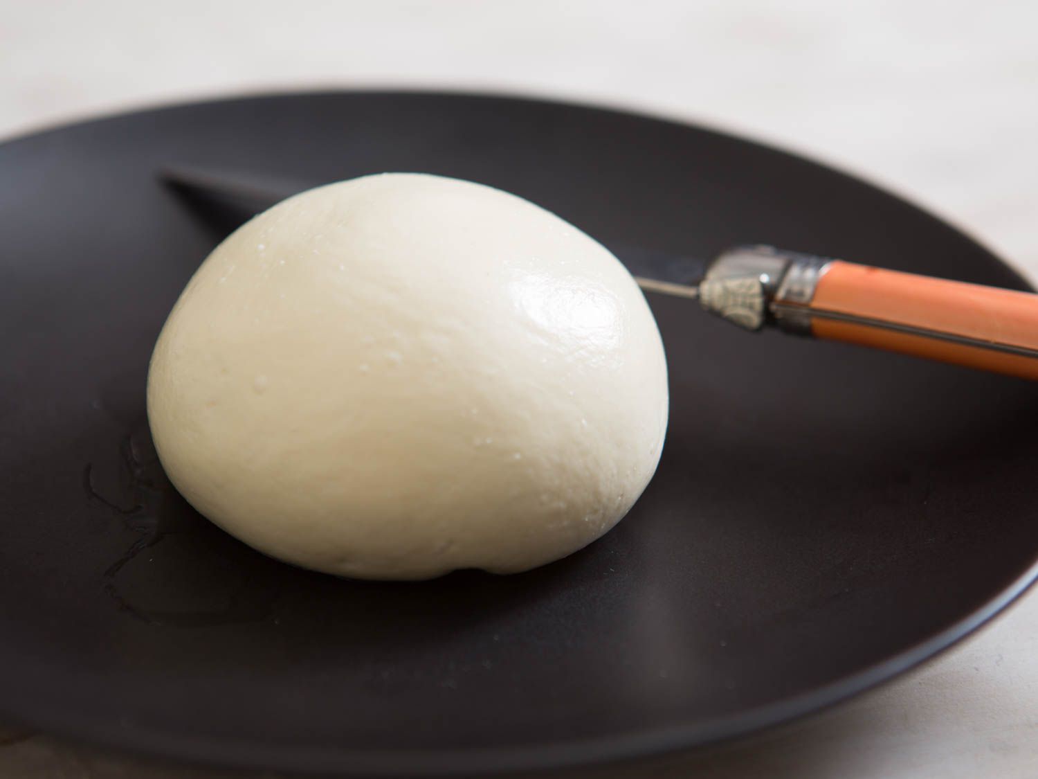 Ball of homemade fresh mozzarella on a black plate with a knife in the background.