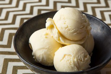 A small black bowl of scooped buttermilk ice cream, set on a surface with a bronze and white zig-zag pattern.