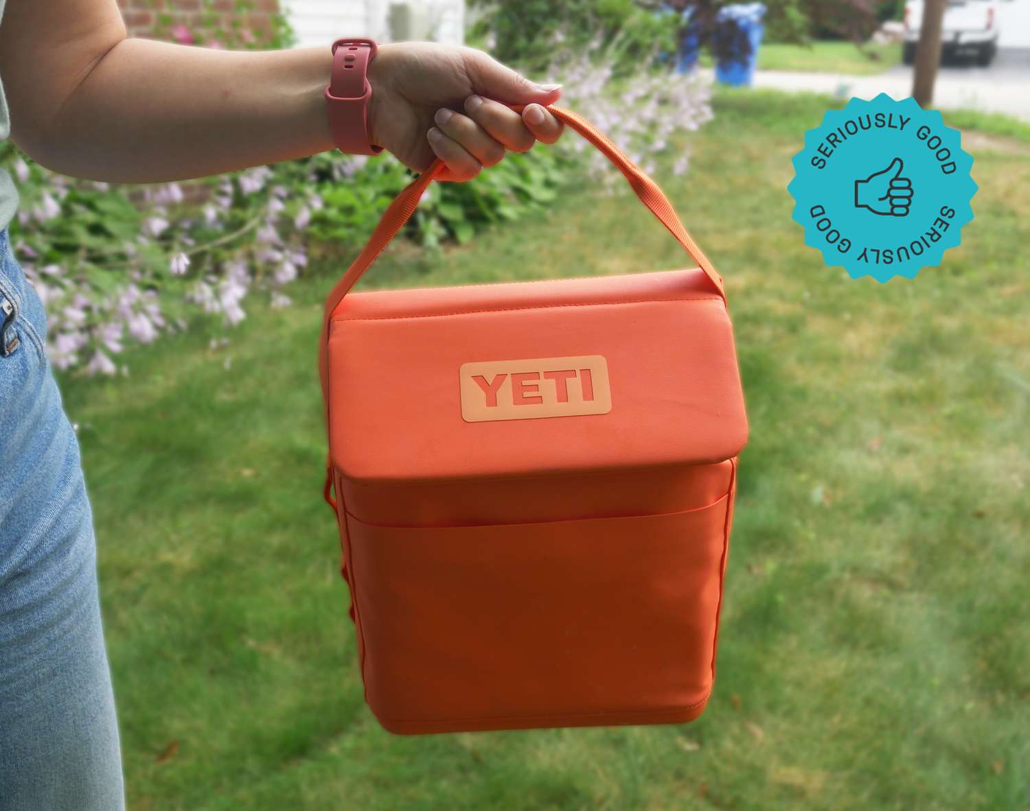 a person holding the handle on a bright orange yeti daytrip lunchbox 