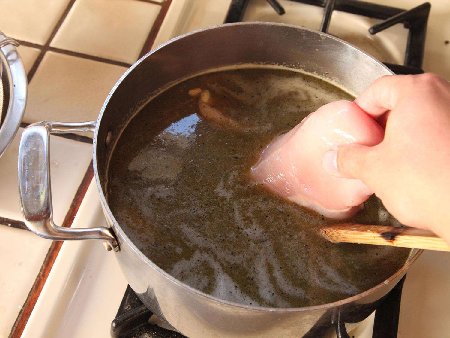 Adding chicken breast into a pot with stock and chile puree.