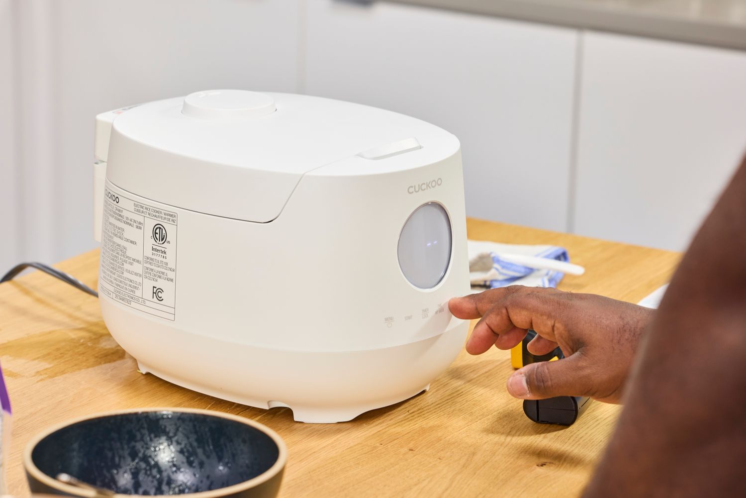 A person presses a button on the Cuckoo 6-Cup Micom Rice Cooker