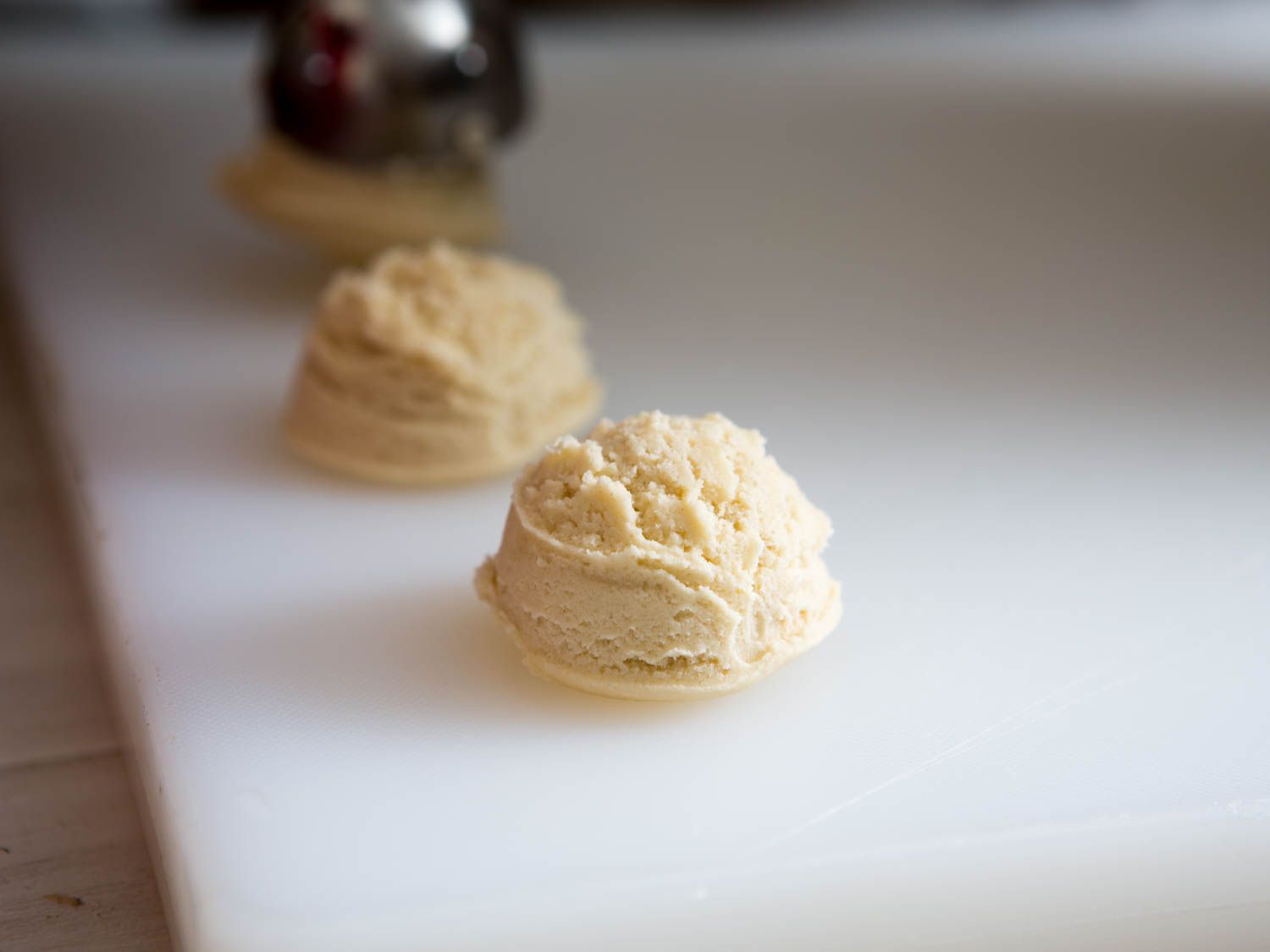 Scoops of raw dough for soft and chewy sugar cookies.