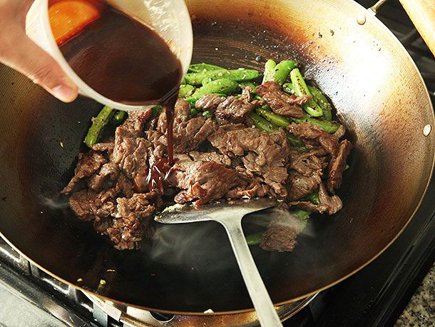Stir fried snap peas and steak in a wok with sauce being poured in.