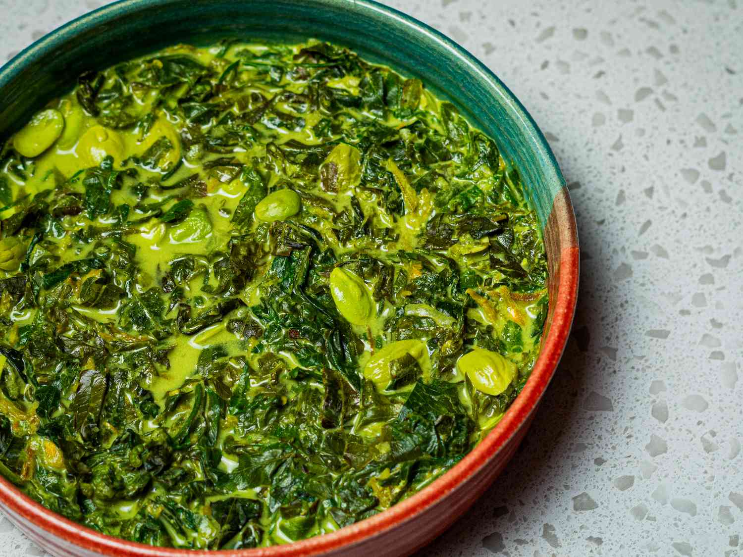 Fiddleheads and fava beans in coconut milk in a bowl.