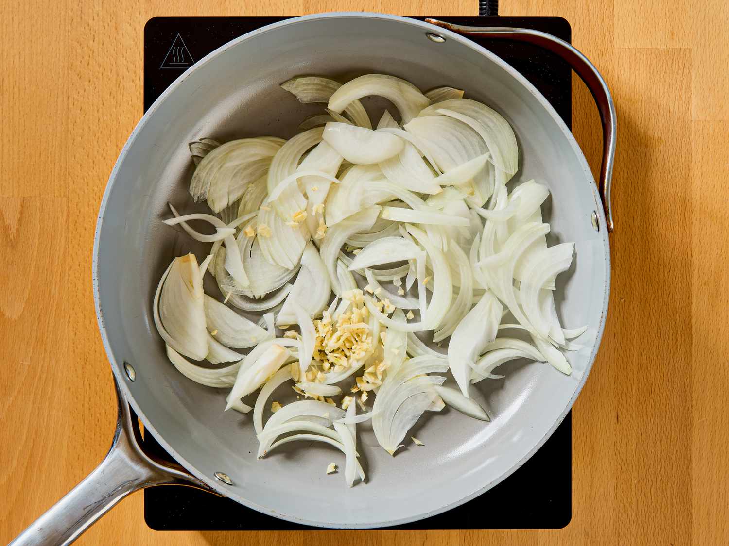 A skillet on a stove containing sliced onions and minced garlic being cooked