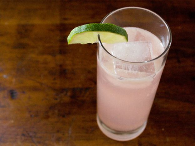 A tall glass with a rhubarb ginger cocktail garnished with a lime wedge.