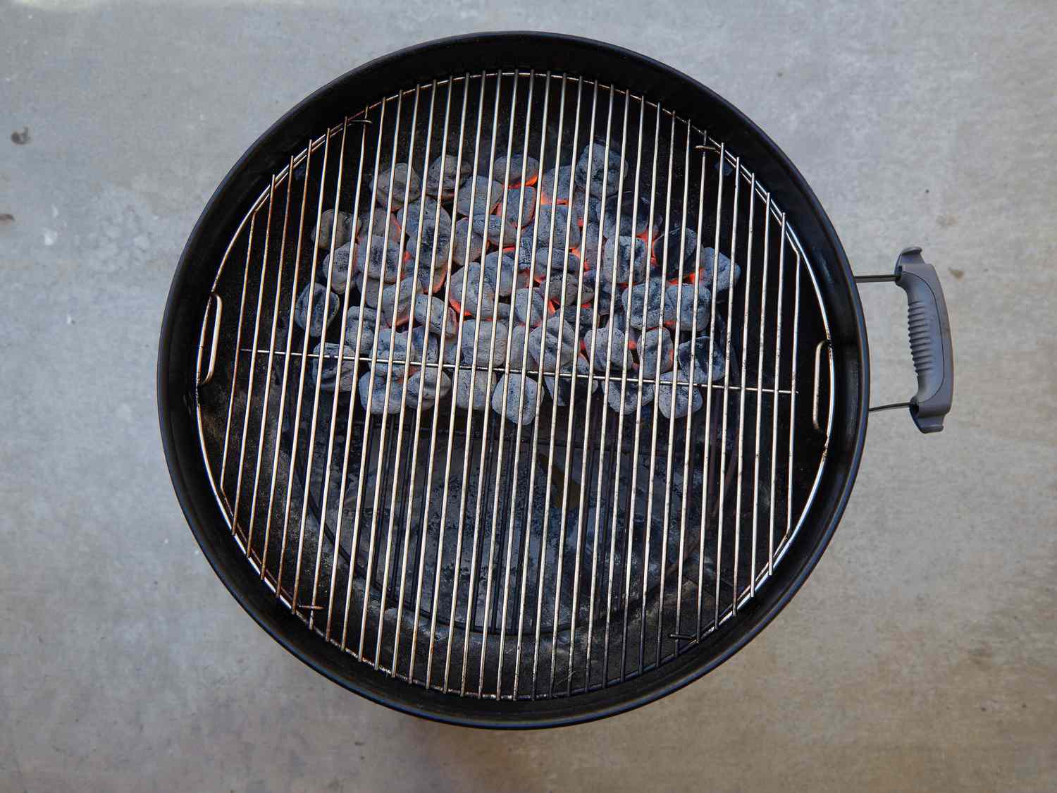 A grill with burning charcoal briquettes arranged in the center under the grate