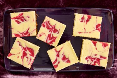 Strawberry cheesecake bars in a purple tray, on purple velvet 