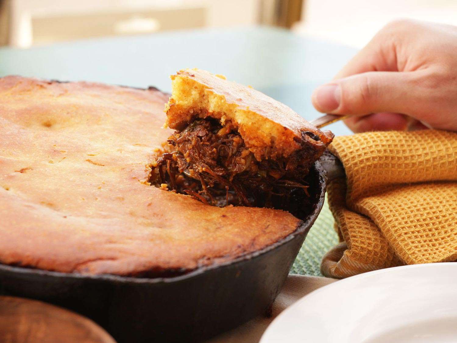 Hand lifting spoonful of tamale pie from cast iron skillet
