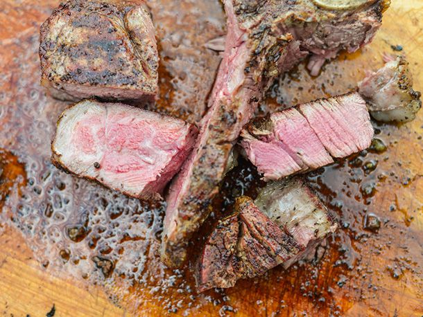 Overhead of the second, reverse-seared steak sliced up on a cutting board. Chunks of the strip loin and tenderloin have been propped up next to the T-bone so that their interior is visible.