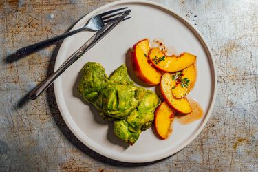 Overhead view of yogurt- and mint-marinated chicken thighs, served on a white plate with quick-pickled nectarine segments.