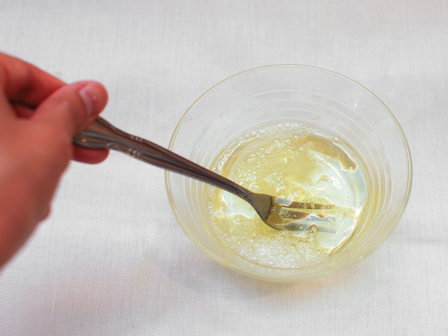 Egg whites being beaten with a fork in a small glass bowl.