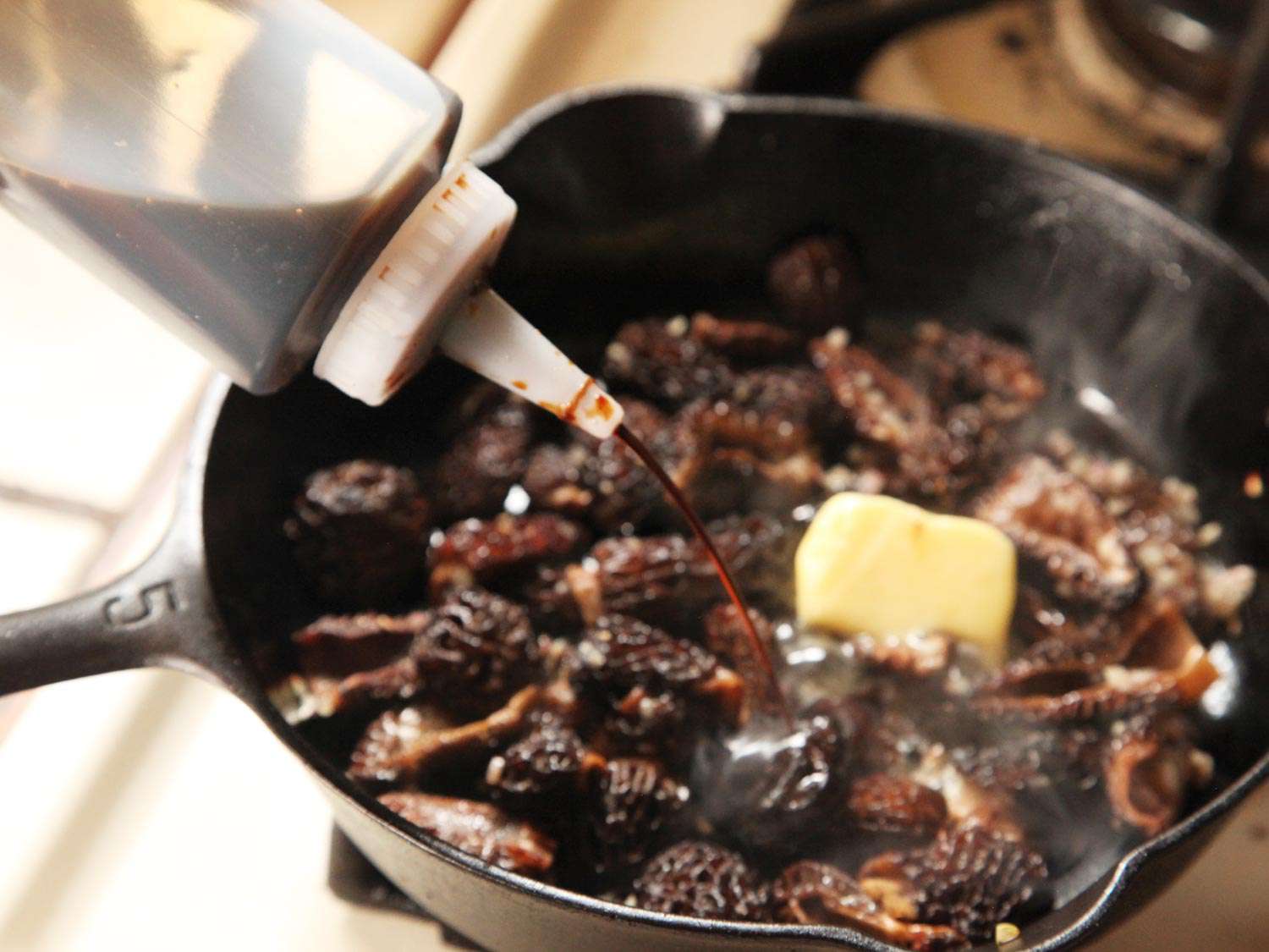 Squirting soy sauce into a pan of sautéed morels with a pat of butter on top.