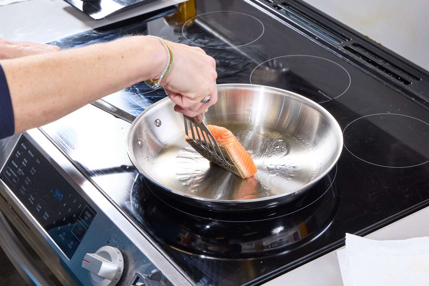 A person flips a piece of salmon on the All-Clad D3 Stainless-Steel 12-Inch Fry Pan