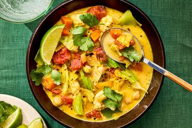 A bowl of cabbage soup with lime wedges and a spoon