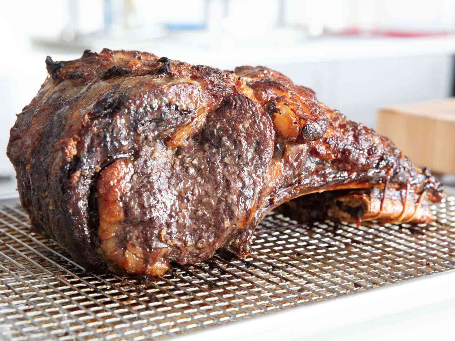 A whole cooked prime rib roast resting on a wire rack. 