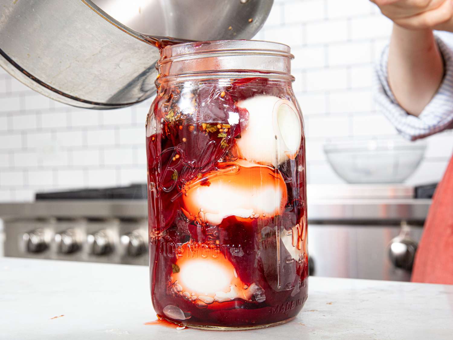 Pouring pickling liquid into jar with eggs and beets