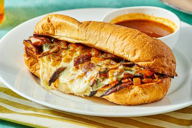 Vegetarian French dip sandwich with cheese and grilled vegetables on a platter, served with a cup of dipping broth