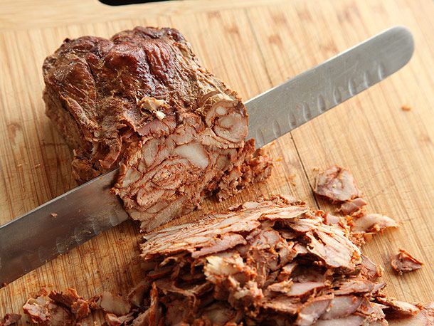 Roasted al pastor loaf being sliced thin with a carving knife
