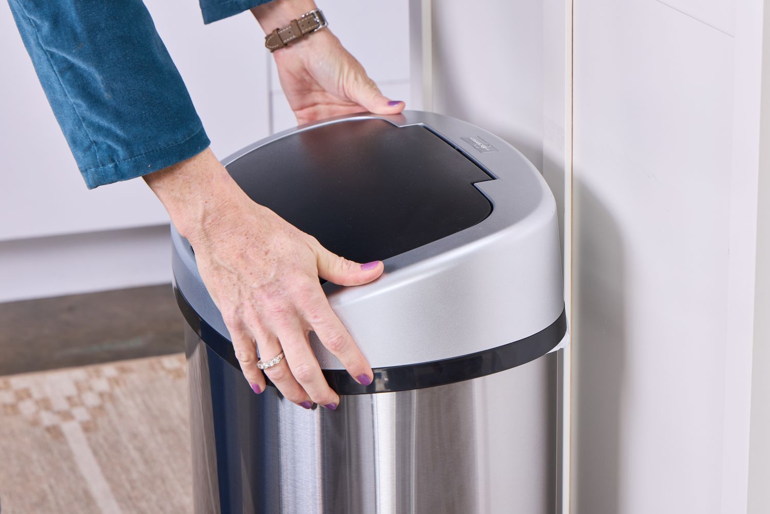 A person places a lid on the iTouchless 13-Gallon Oval Stainless Steel Sensor Trash Can