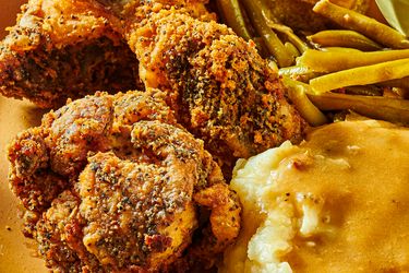 Dish of fried chicken with coleslaw, greenbeans, and mashed potatoes, with a fork and serving dishes in the background
