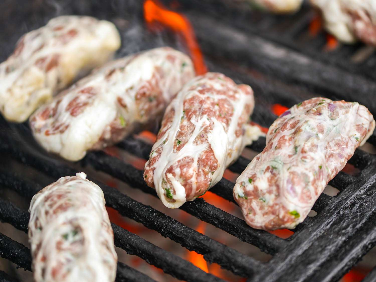 Sheftalia are arranged on a grill grate to cook.