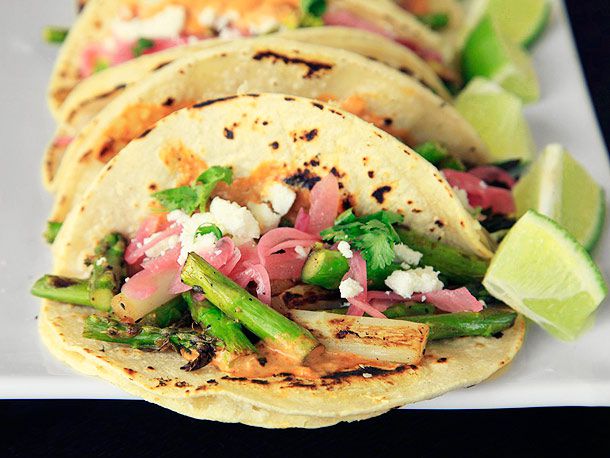 Closeup of Charred Asparagus Tacos With Creamy Adobo and Pickled Red Onions, served with lime wedges.