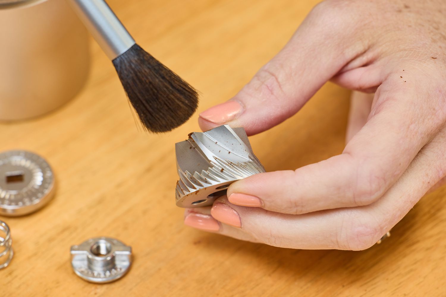 A person brushes a part from the 1Zpresso J Manual Coffee Grinder
