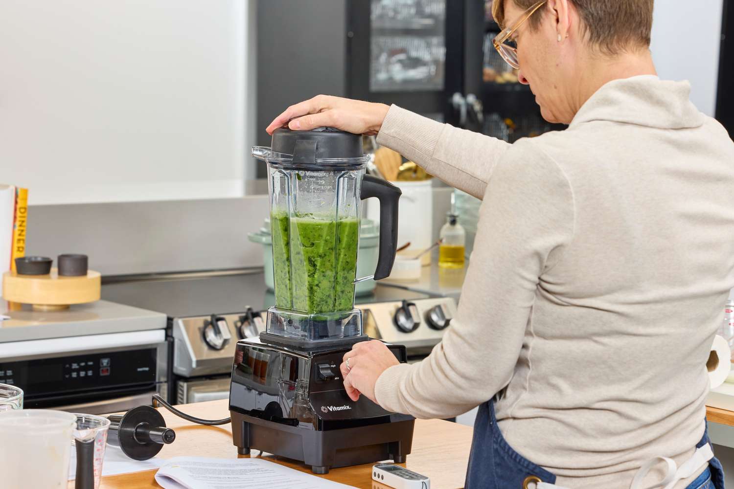 A person using the Vitamix 5200 Professional-Grade Blender on a wooden counter to blend green items