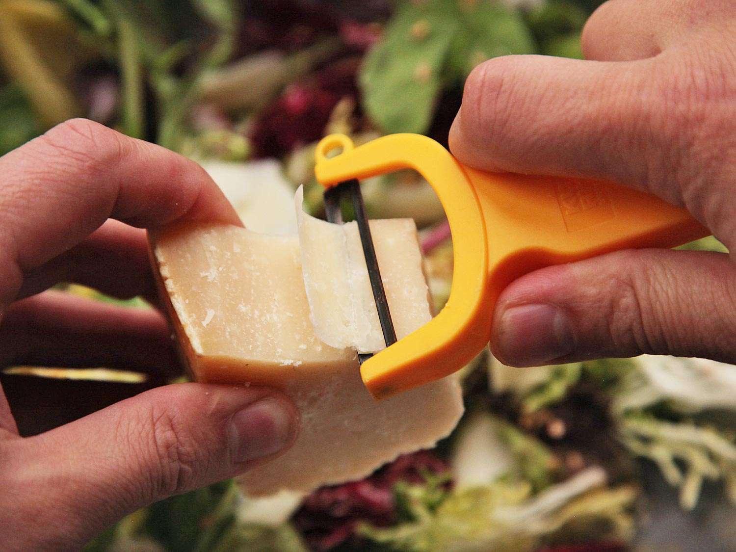 The author shaves parmesan from a block with a Y-peeler.