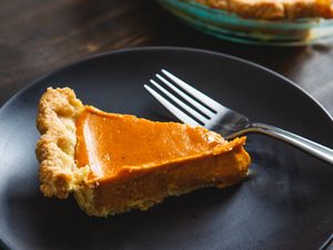 Slice of pumpkin pie on a plate with a fork next to it
