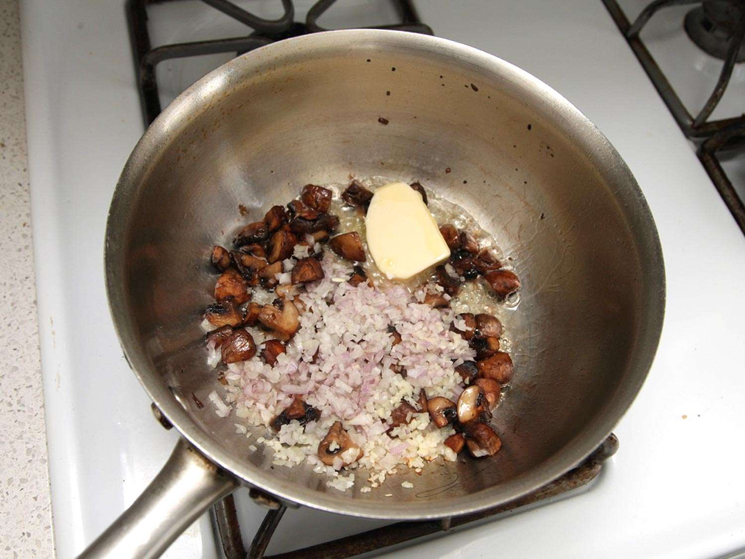 Adding minced shallots to browned mushrooms.
