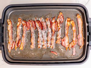 An electric griddle filled with bacon cooking.