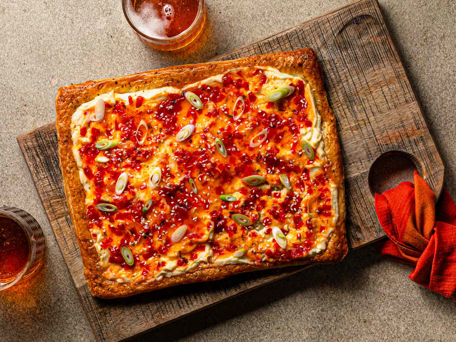 A cheese and pepper jelly tart garnished with green onions on a wooden board