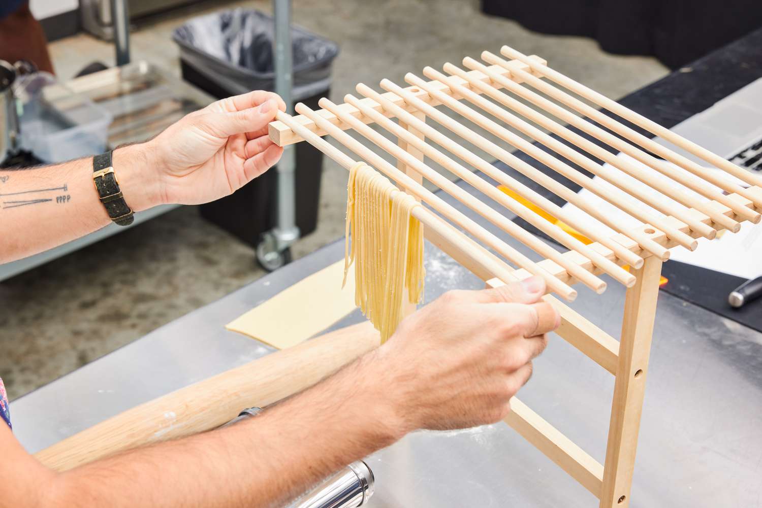 Person adjusting CucinaPro Pasta Drying Rack with pasta noodles hanging on one dowel