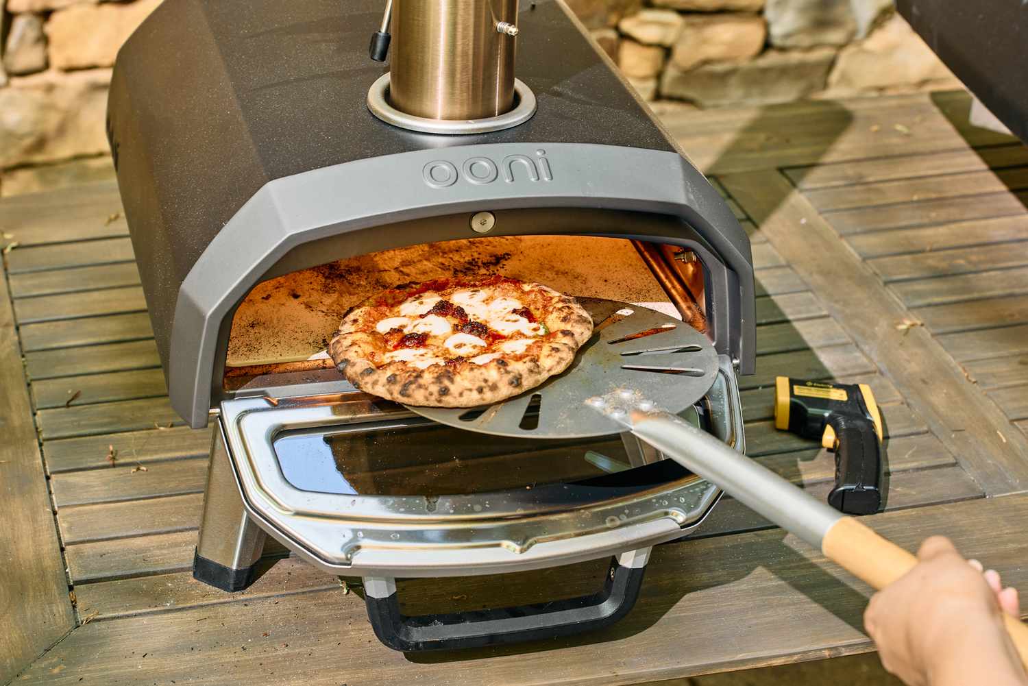A person removes a pizza from the Ooni Karu 2 Multi-Fuel Pizza Oven