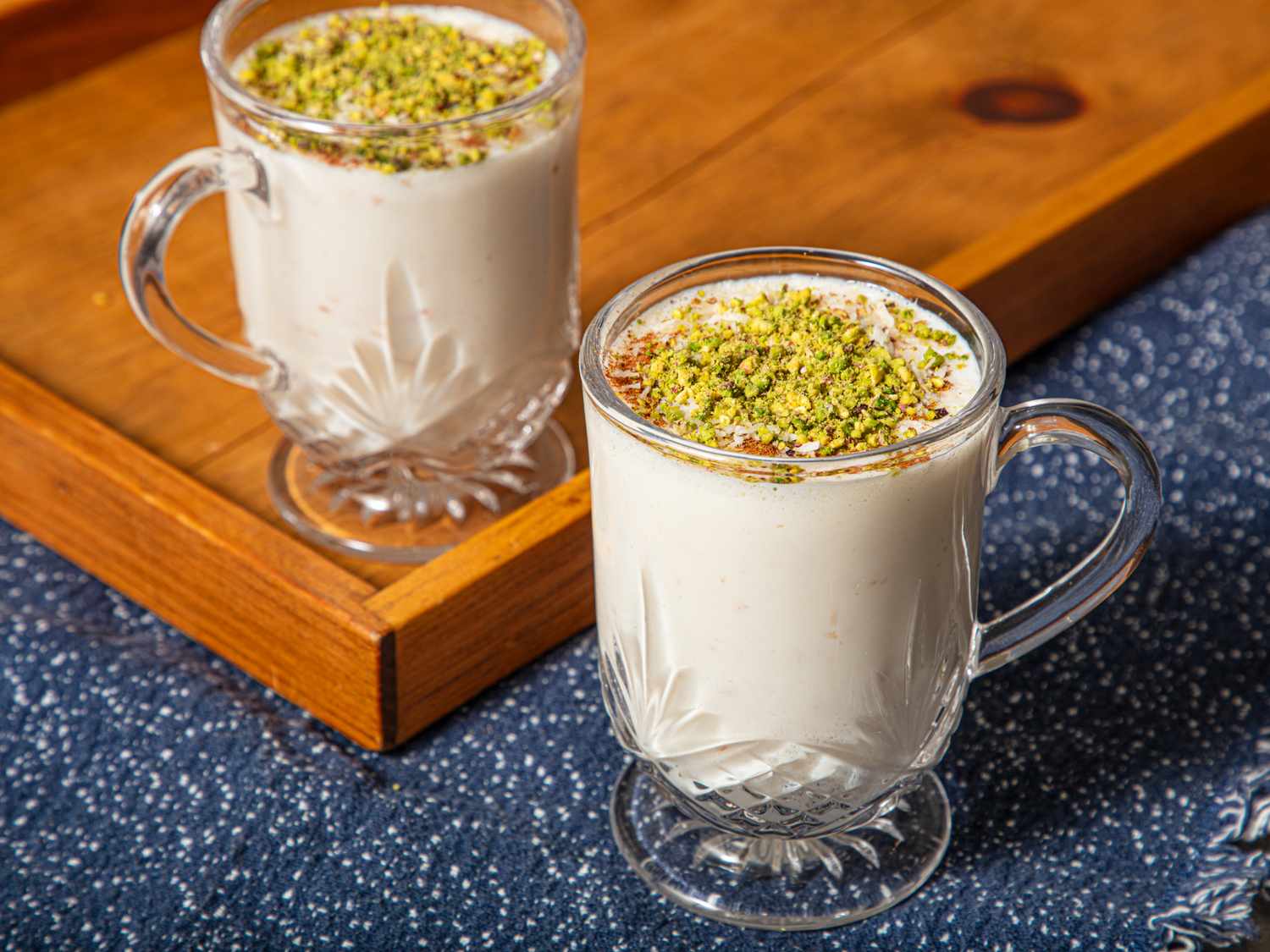 Two cups of sahlab topped with chopped nuts on a wooden tray