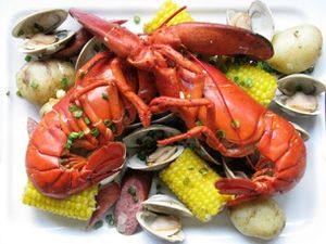 Overhead view of a lobster boil arranged on a square white porcelain platter.