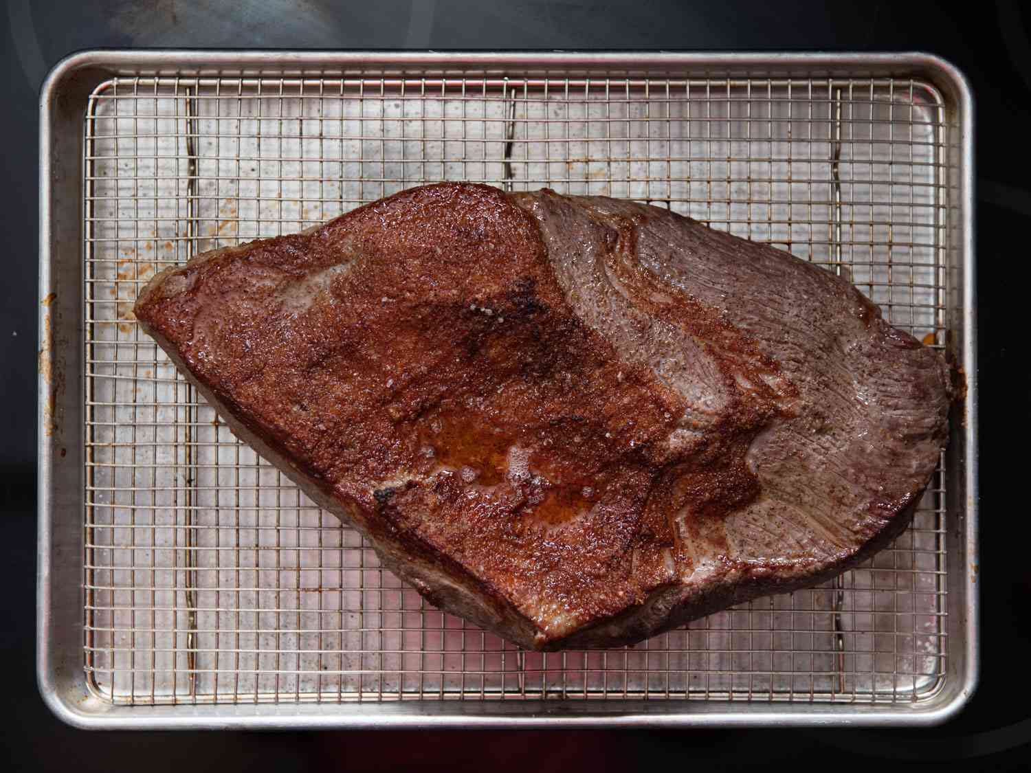 Overhead shot of cooked brisket on a wire rack in a rimmed baking sheet