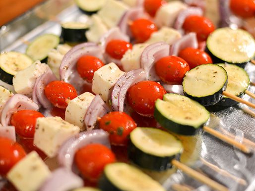 Skewers with zucchini, halloumi, red onion, and cherry tomatoes lined up next to each other.